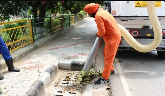 Sanitation worker using a vacuum machine to clean roadside leaves and debris
